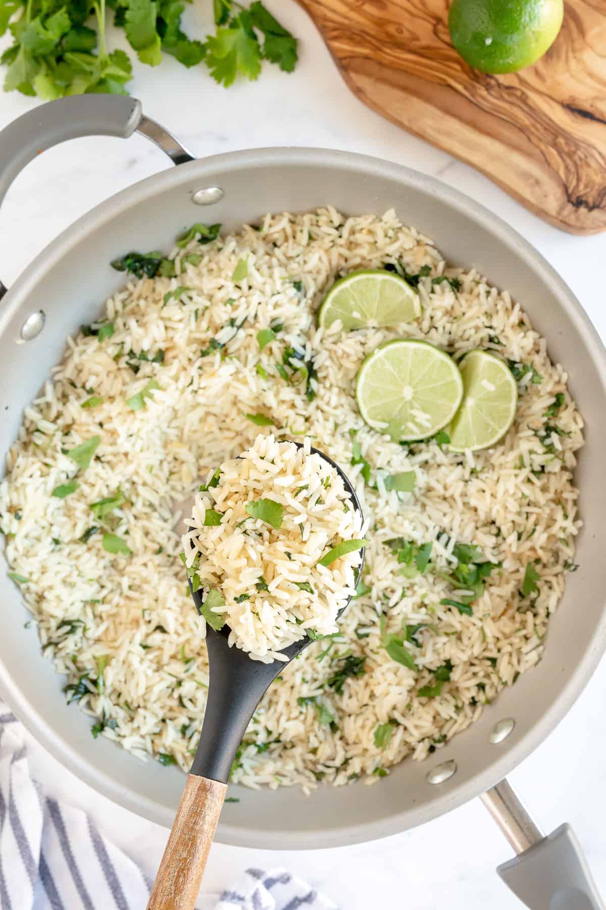 A skillet filled with rice with cilantro and slices of lime.