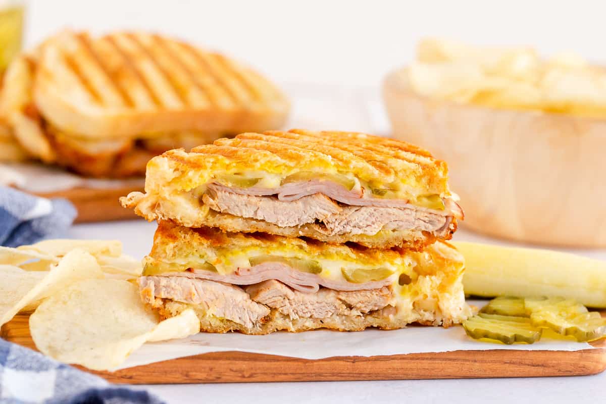 A cuban sandwich on a plate with potato chips and pickles.