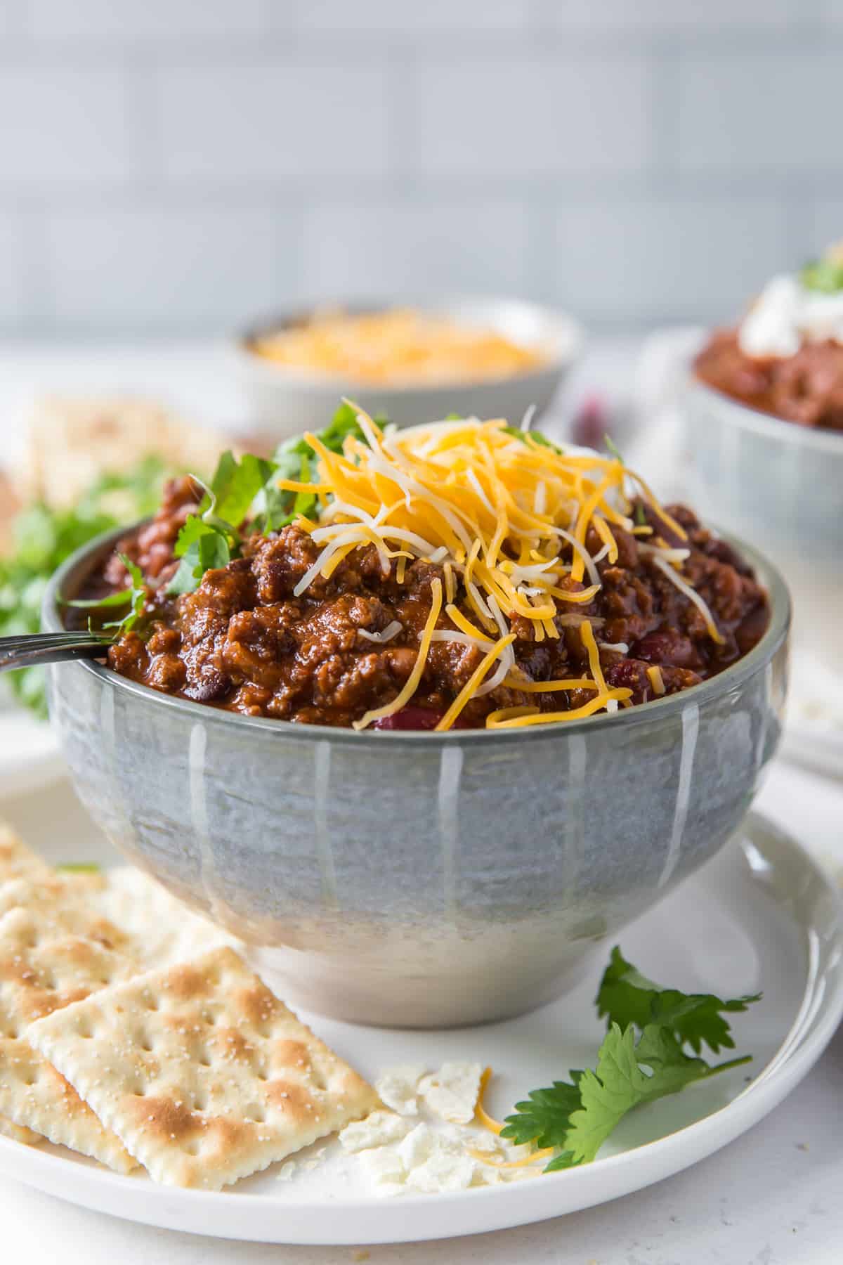 A bowl of chili on a plate with saltine crackers.