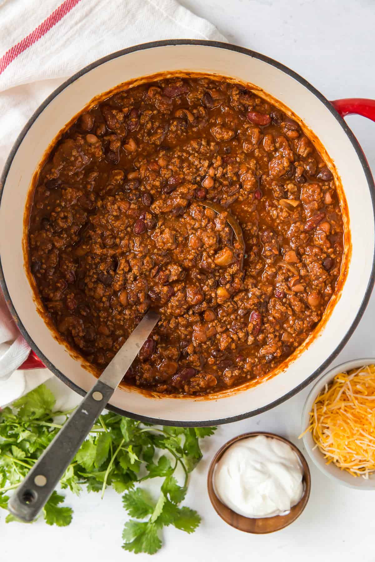 A ladle rests in a pot of chili with toppings set around it.