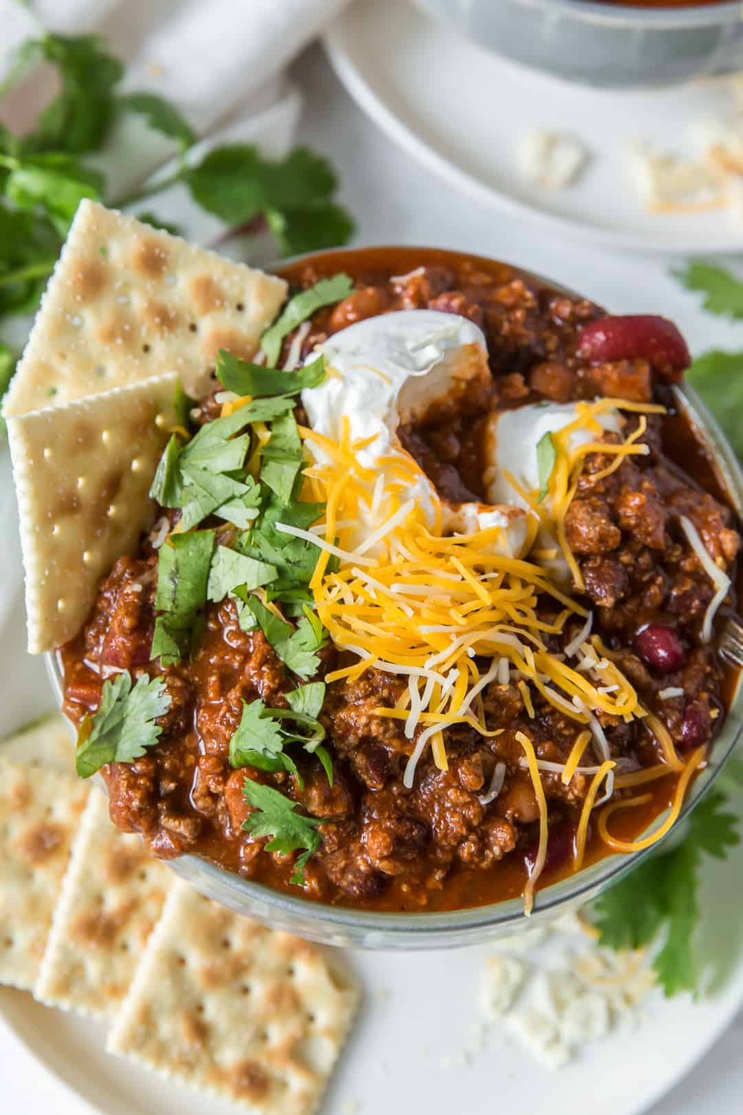 A bowl of beer chili with cheese, sour cream, and saltine crackers.