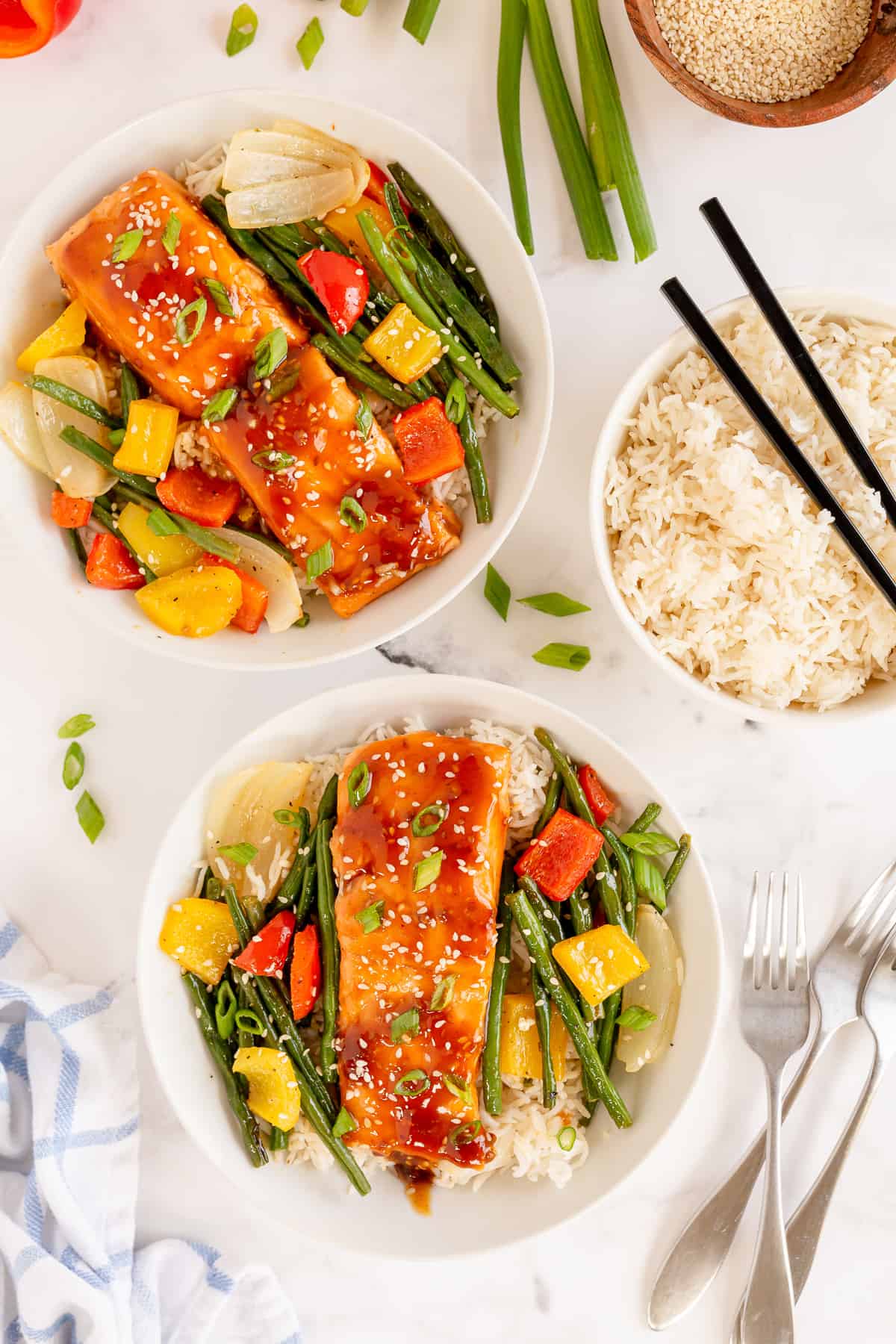 Two bowls filled with vegetables and salmon teriyaki on rice.