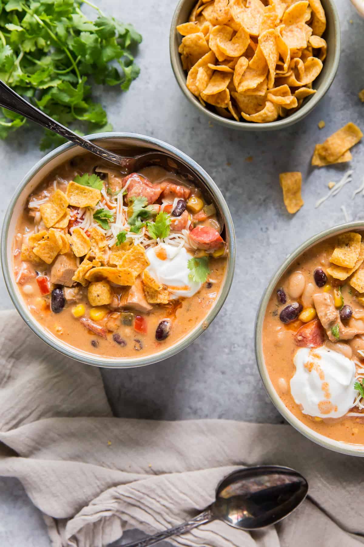 Two bowls of soup next to a bunch of cilantro and a bowl of fritos.