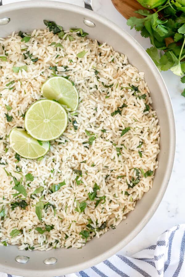Skillet filled with fluffy Cilantro Lime Rice garnished with fresh cilantro and lime slices.