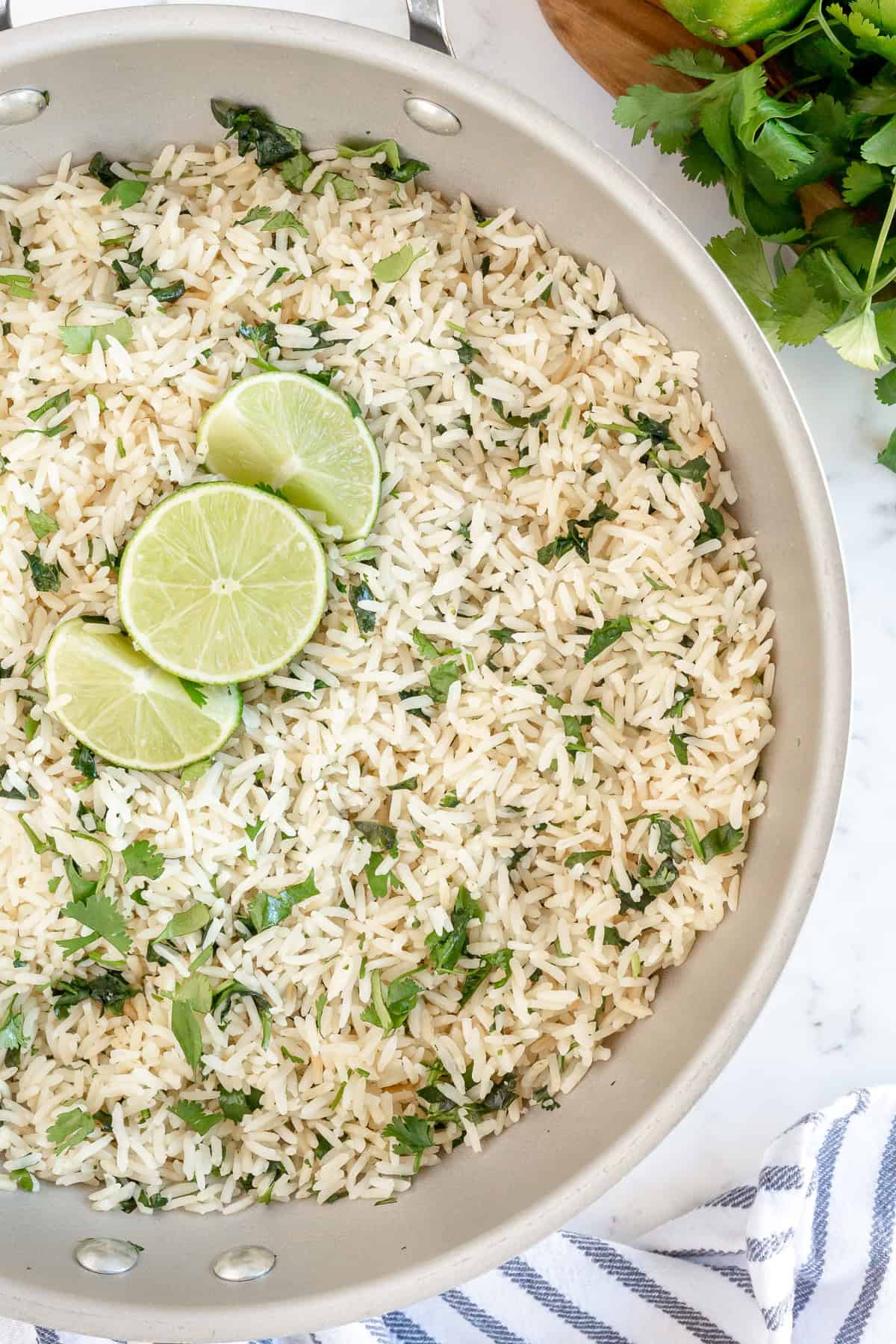 Skillet filled with fluffy Cilantro Lime Rice garnished with fresh cilantro and lime slices.