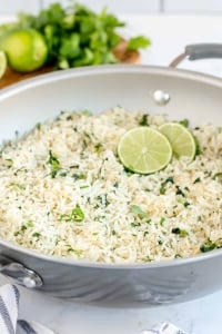 A skillet filled with white rice, cilantro and lime slices.