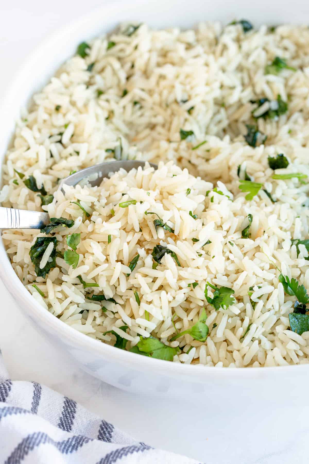 A spoon scoops Cilantro Lime Rice from a white serving bowl.