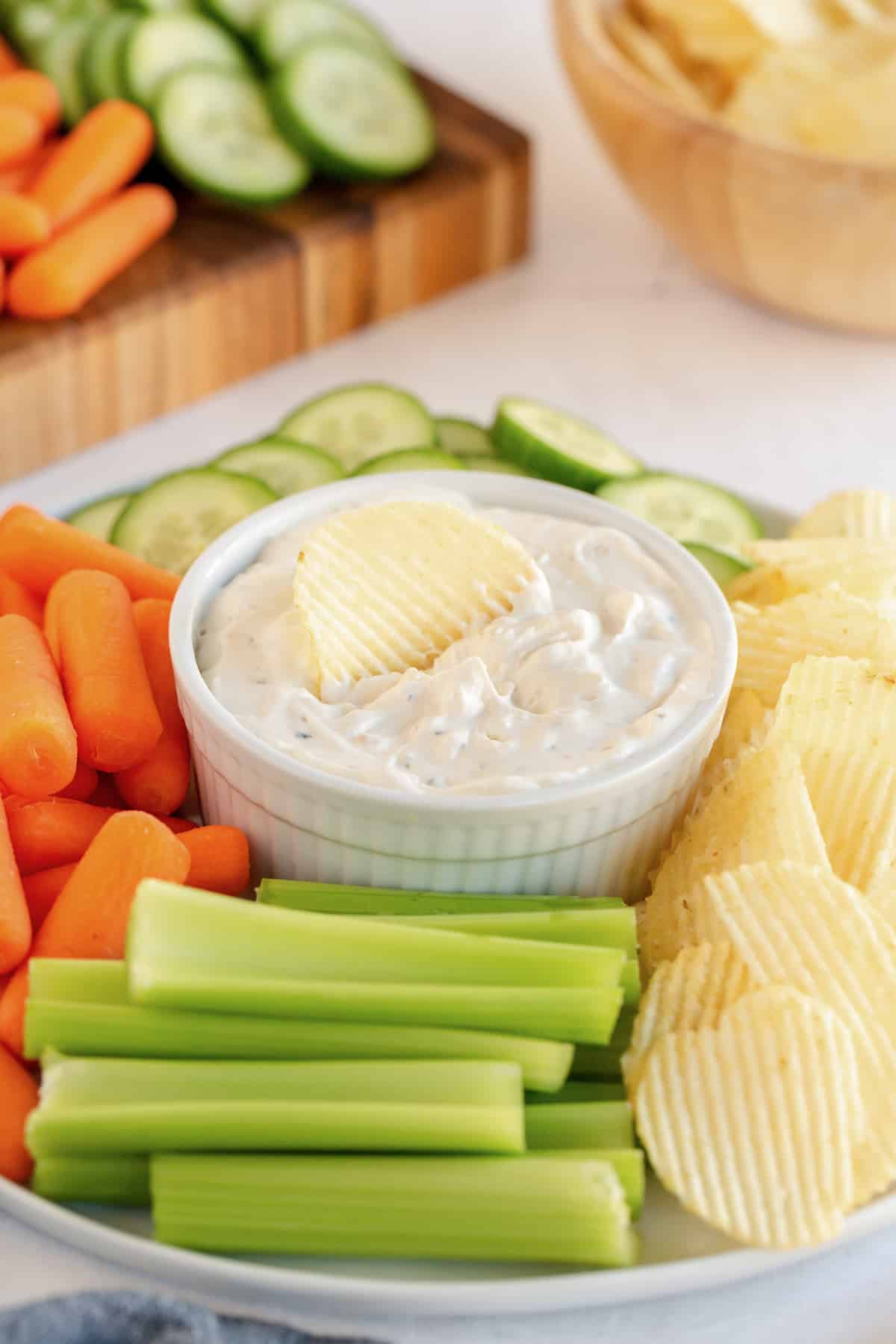 A platter of vegetables and potato chips with dip in the center.