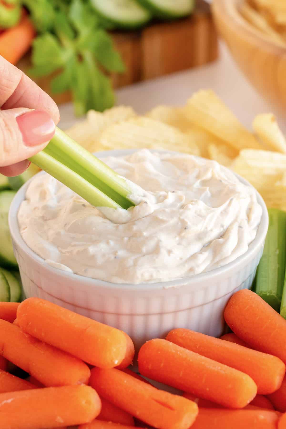A hand dipping celery into onion dip.