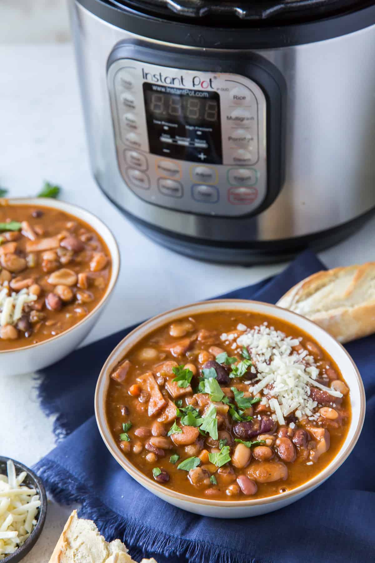 A bowl of bean soup on a blue cloth in front of an Instant Pot.