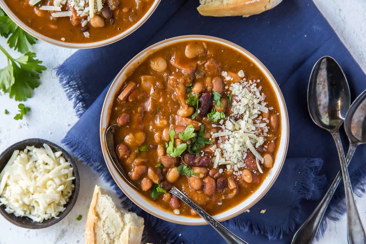 A bowl of bean soup next to a smaller bowl of shredded cheese.