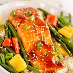 A bowl filled with rice, vegetables and teriyaki salmon.