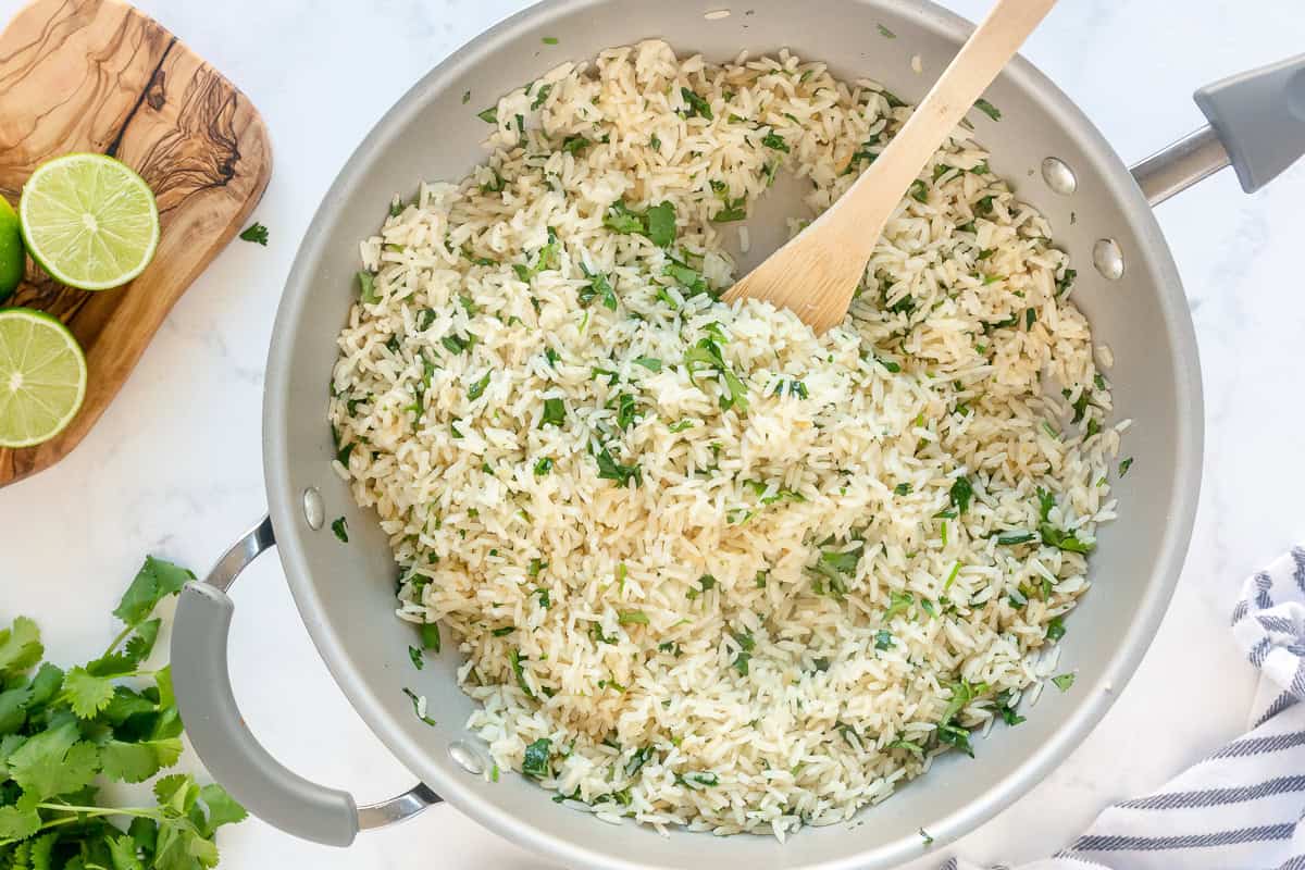 Cilantro Lime Rice being stirred in a skillet with a wooden spoon, garnished with fresh cilantro and lime.