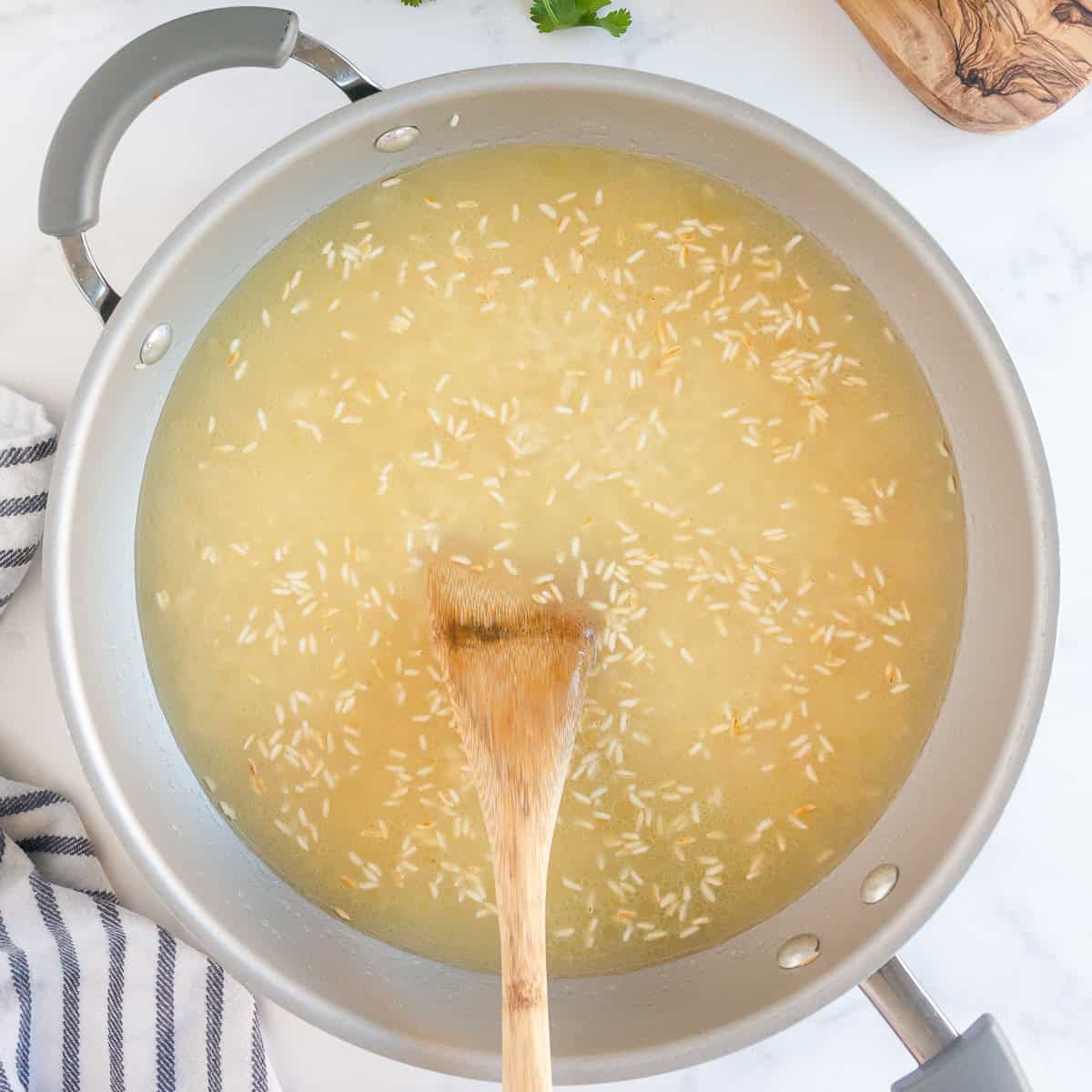 Adding broth to toasted rice to cook cilantro lime rice.