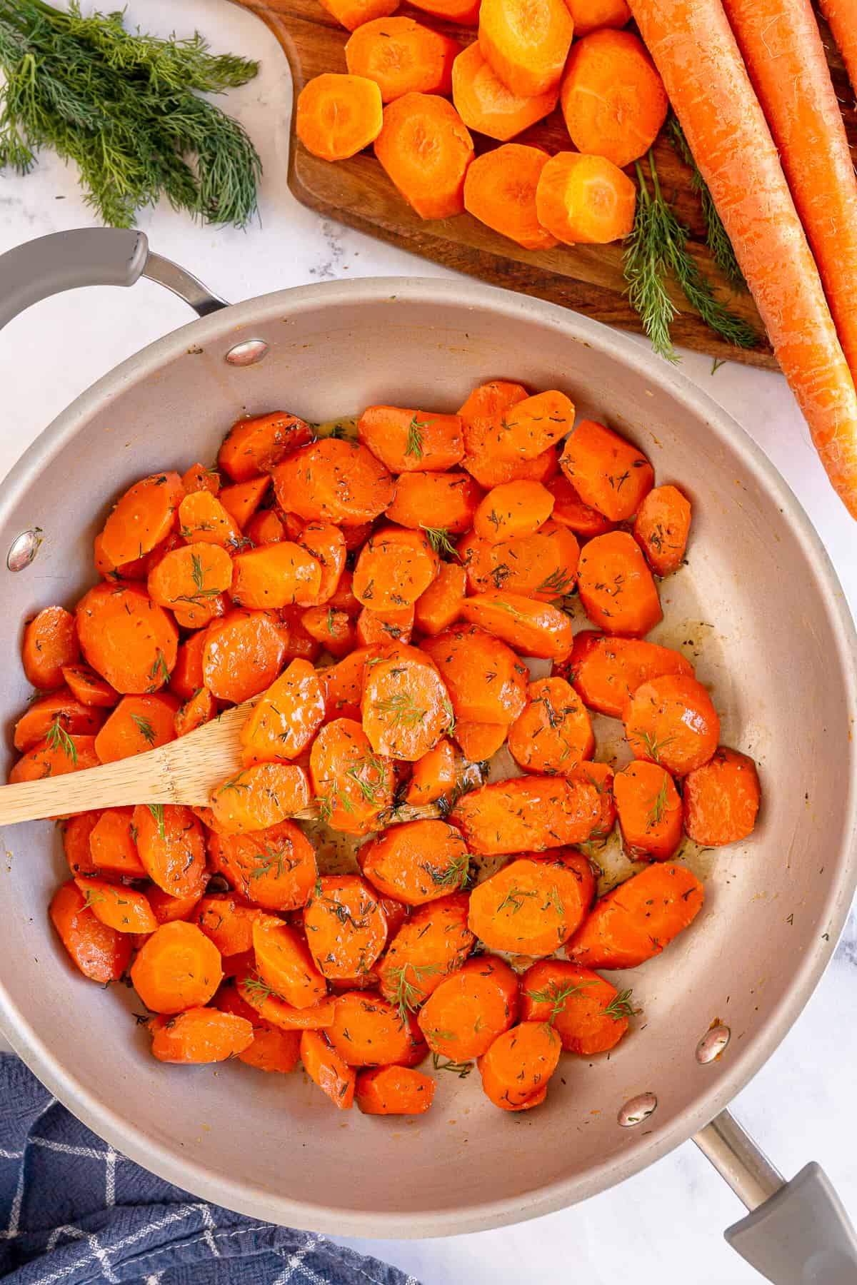 A wooden spoon in a skillet with stovetop glazed carrots.
