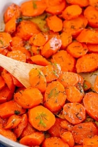 A close up of carrots with dill in a skillet with a wooden spoon.