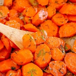 A close up of carrots with dill in a skillet with a wooden spoon.