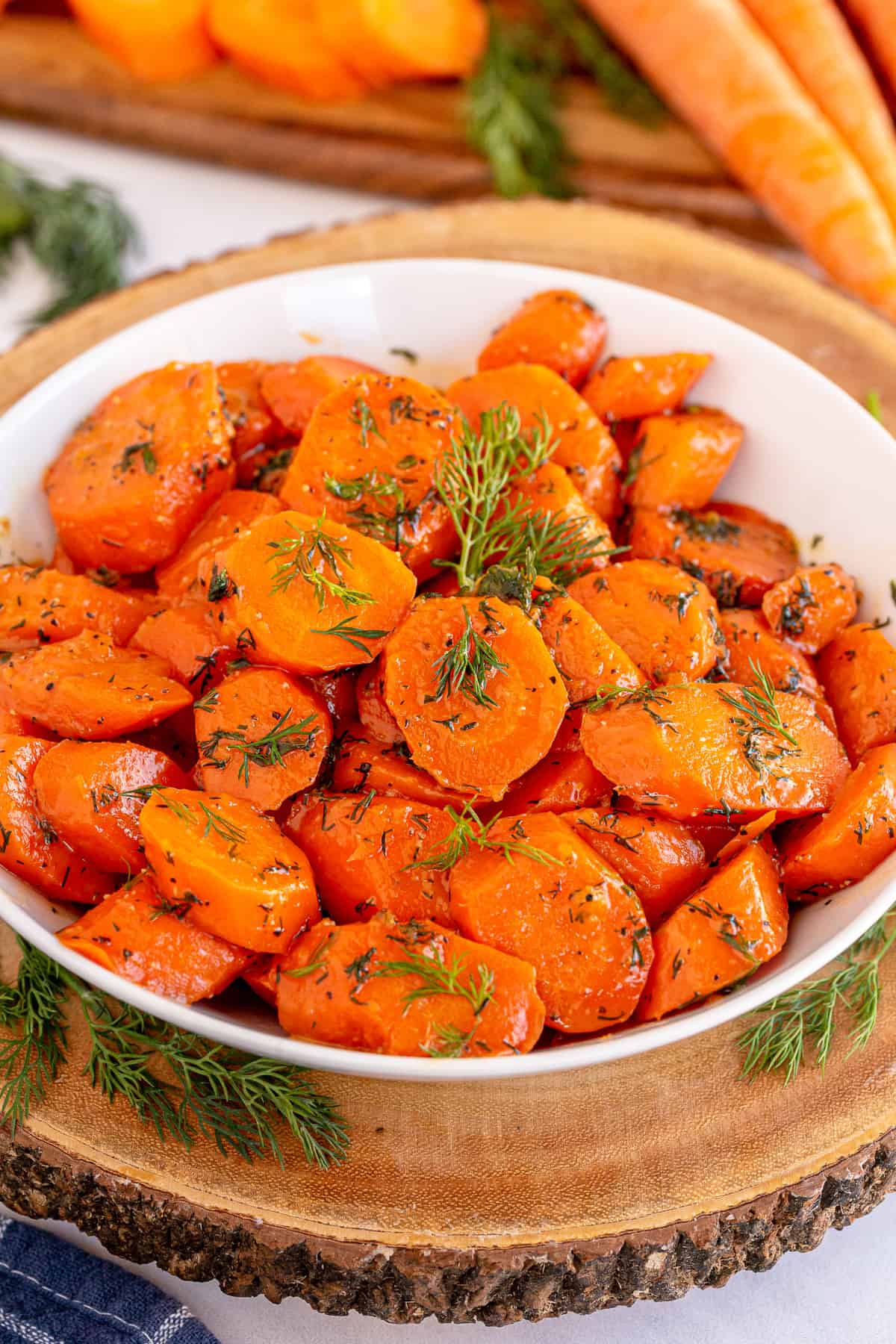 Butter and dill glazed carrots in a white bowl on a wooden block.