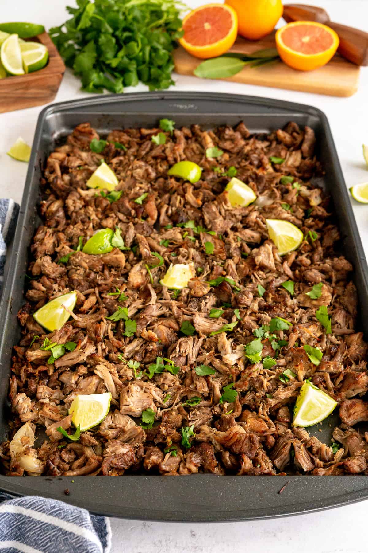 A baking sheet of carnitas with oranges in the background.