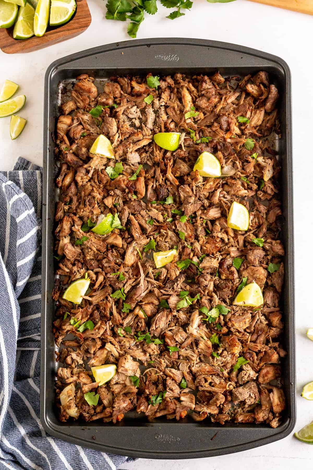 A baking sheet filled with carnitas and pieces of lime.