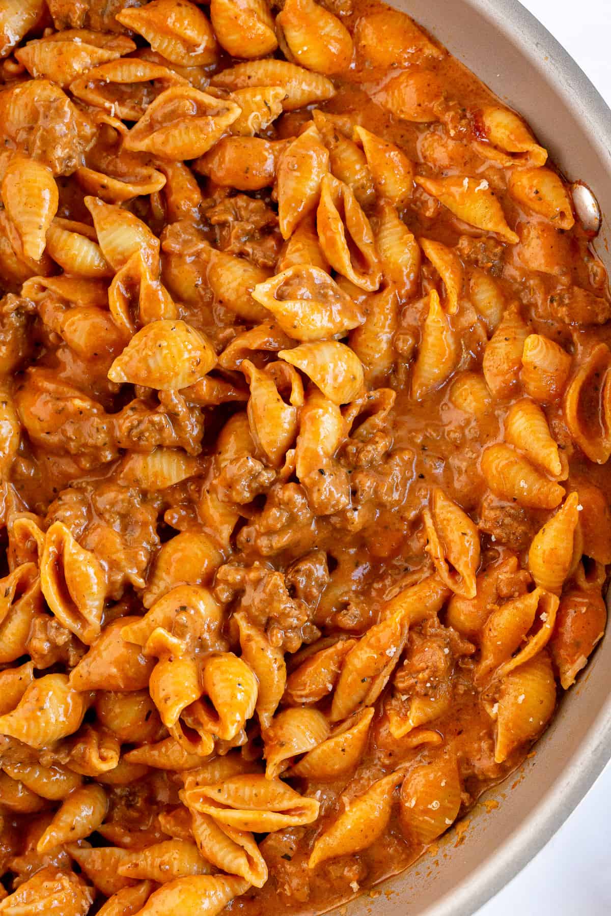 A closeup of a skillet full of pasta shells with a creamy sauce and ground beef.