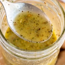 A spoon lifts Italian dressing from a mason jar.