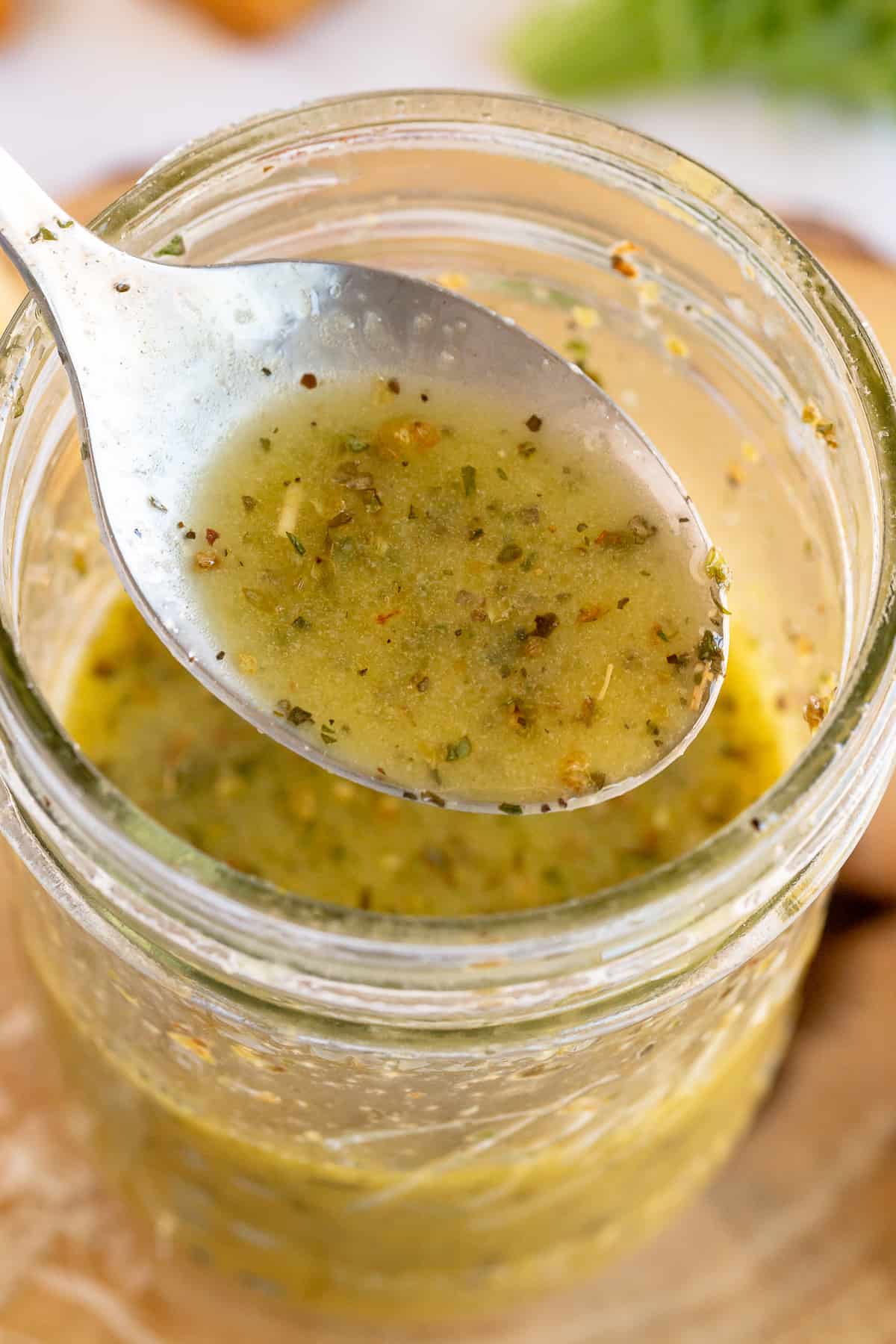 A close up of a spoon lifting salad dressing from a mason jar.