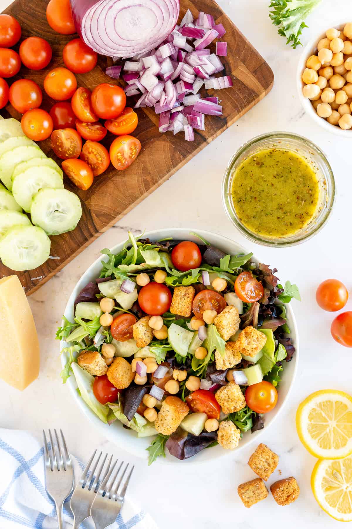 A big colorful salad surrounded by chopped vegetables and Italian salad dressing.