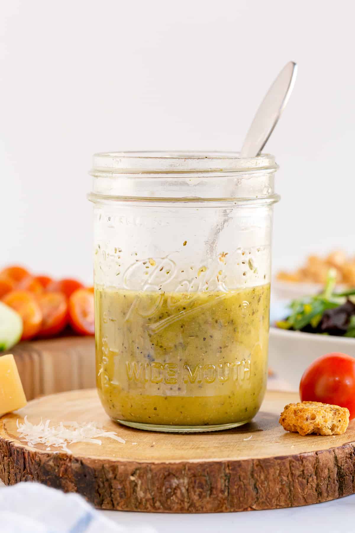 A mason jar filled with salad dressing and a spoon on a wood block.