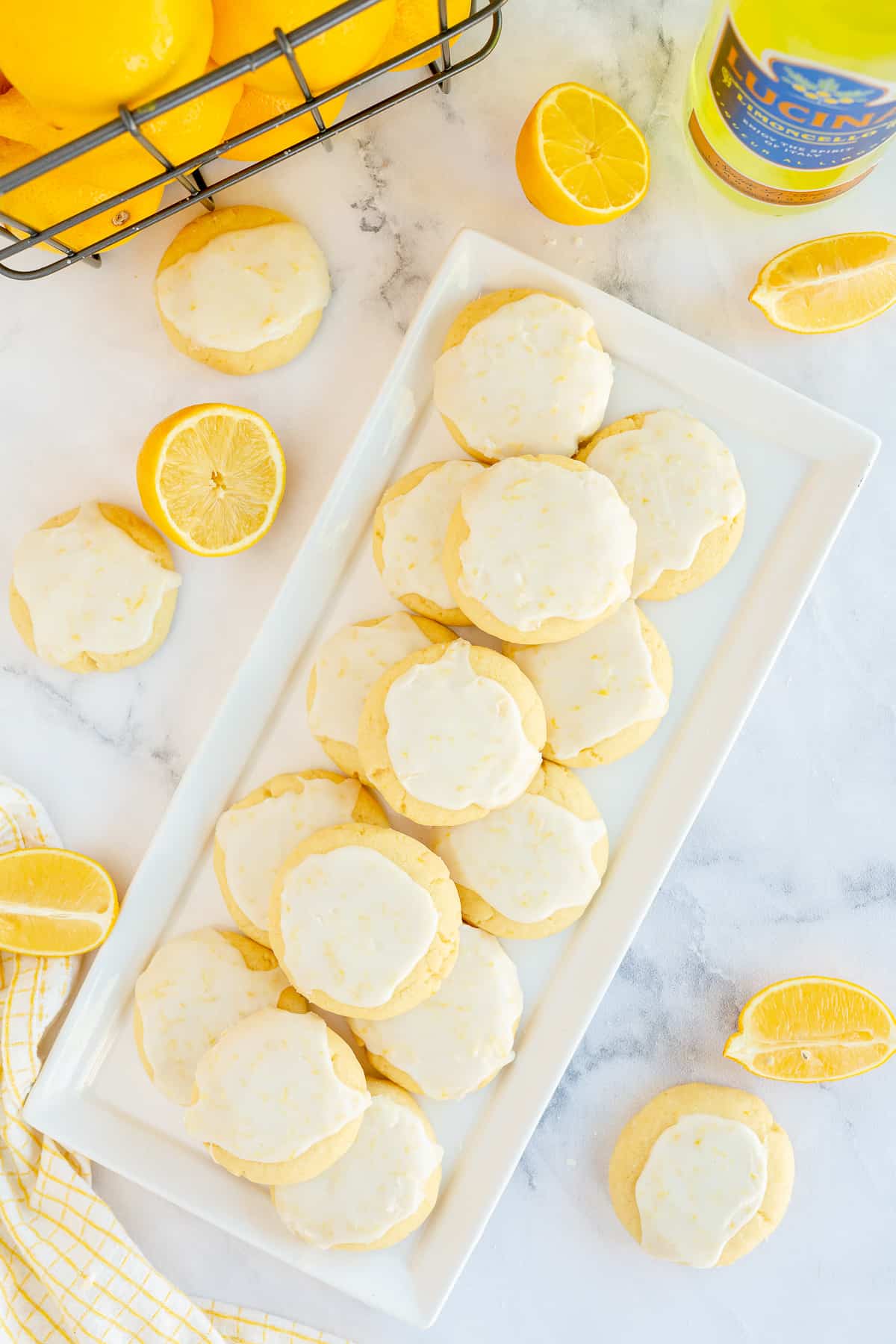A tray of glazed Limoncello Cookies with a basket of lemons behind it shot from over the top.