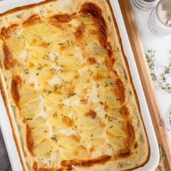 A casserole dish of Scalloped potatoes resting on a cutting board.