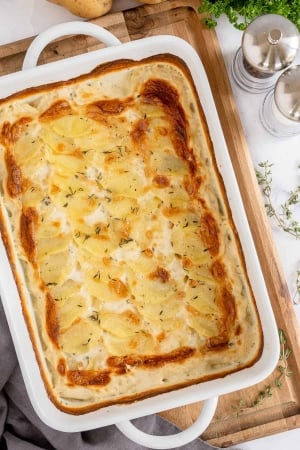 A casserole dish of Scalloped potatoes resting on a cutting board.