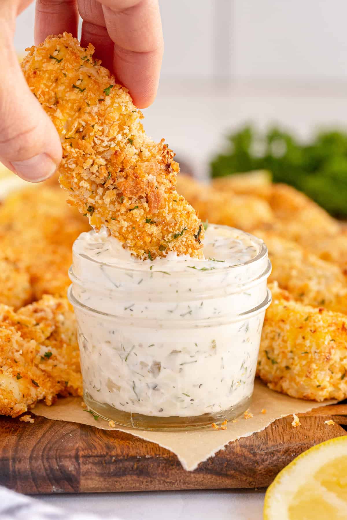 A hand dipping a fish stick into a jar of tartar sauce.