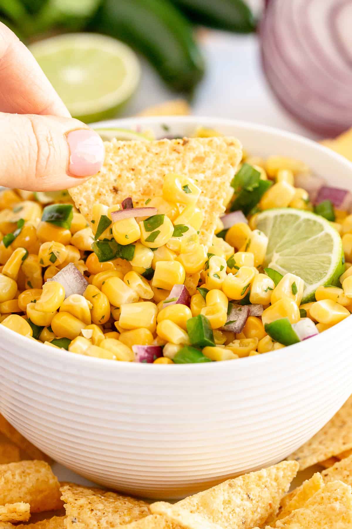 A hand dips a tortilla chip into a bowl of corn salsa.