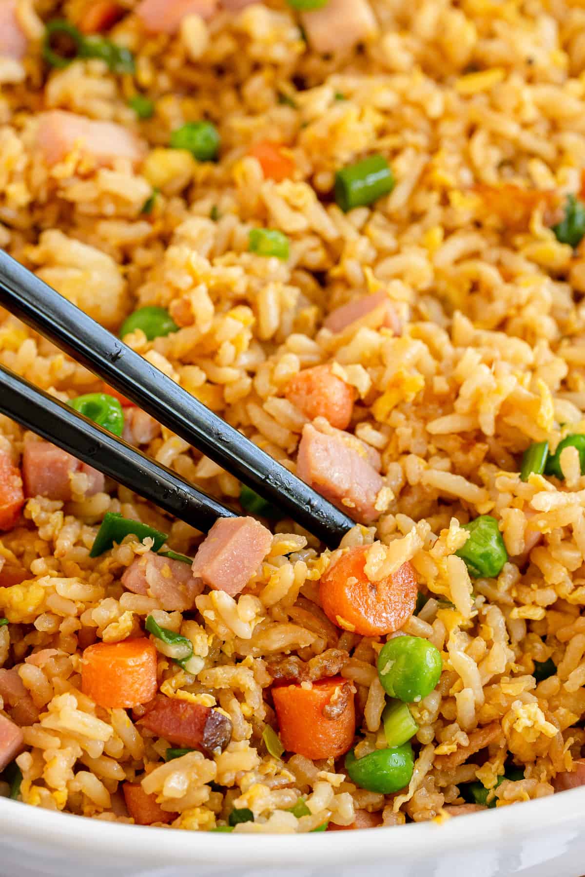 A closeup of chopsticks digging into Ham Fried Rice with carrots and peas.