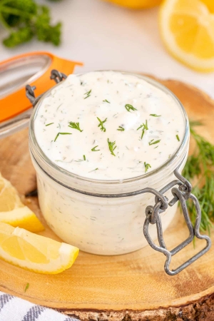 Tartar sauce topped with fresh dill in a small glass jar.