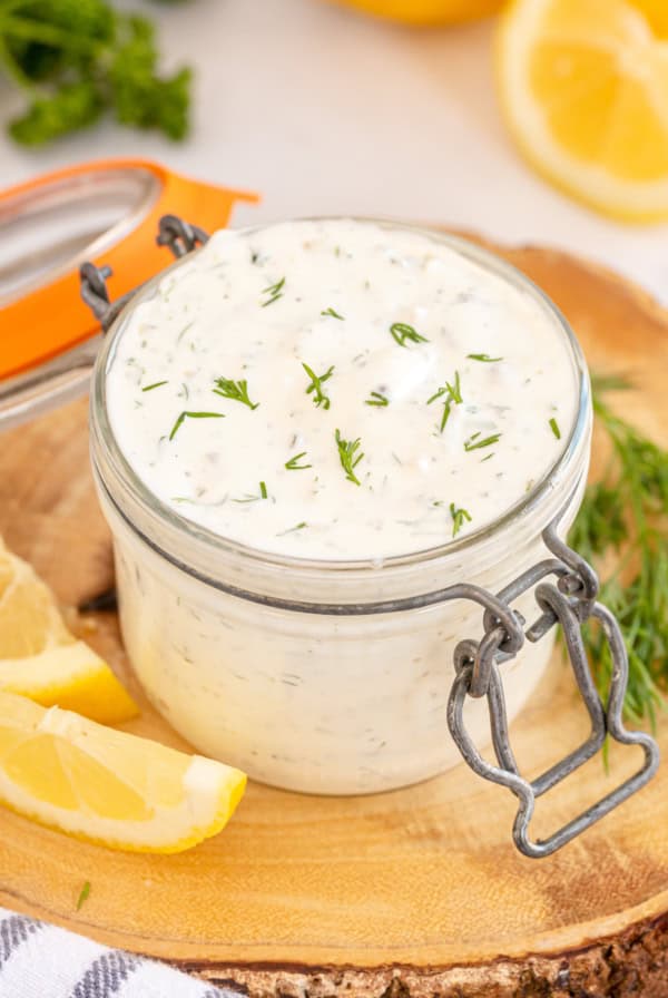 Tartar sauce topped with fresh dill in a small glass jar.