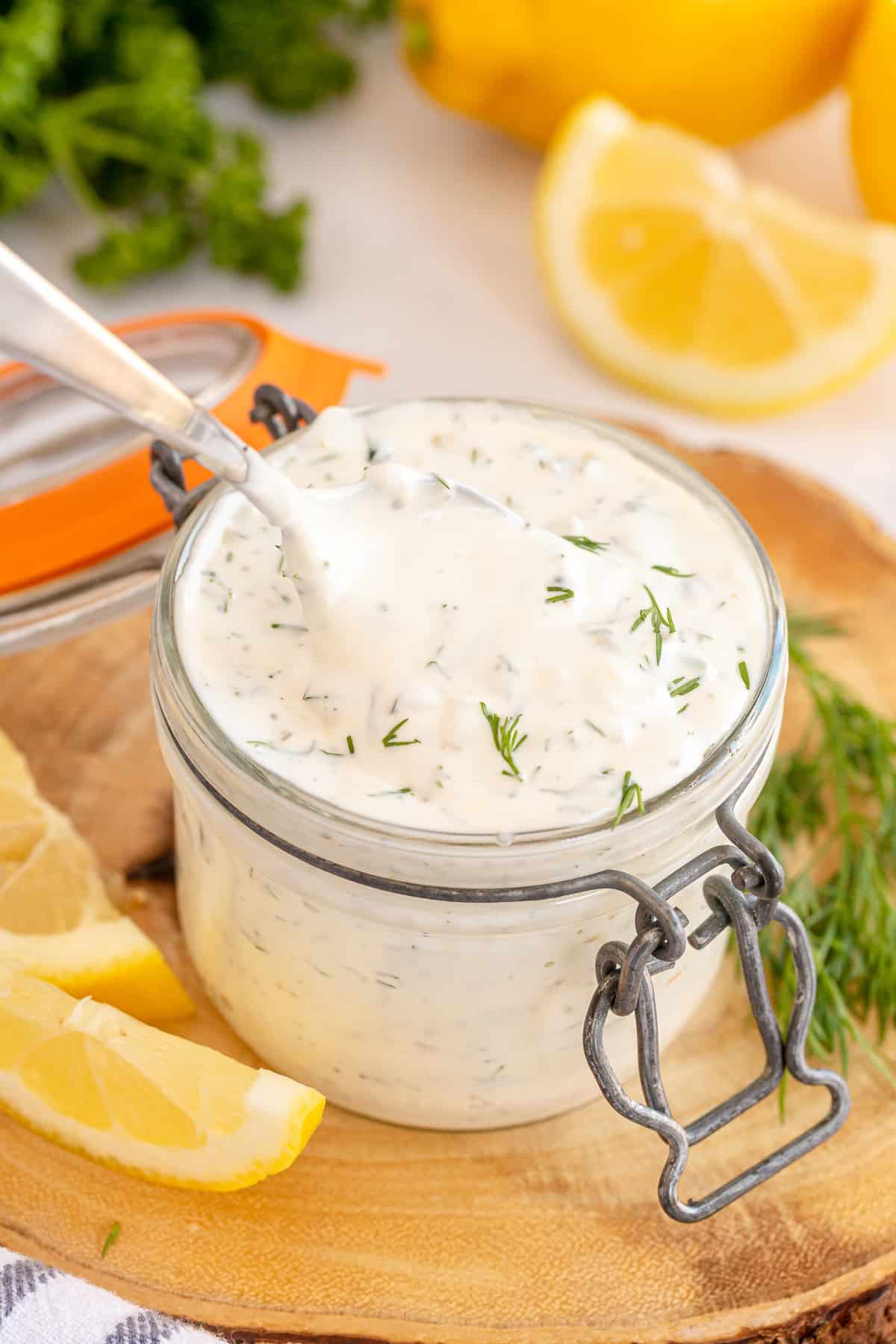 A spoon in a jar of Homemade Tartar Sauce set on a wooden block.