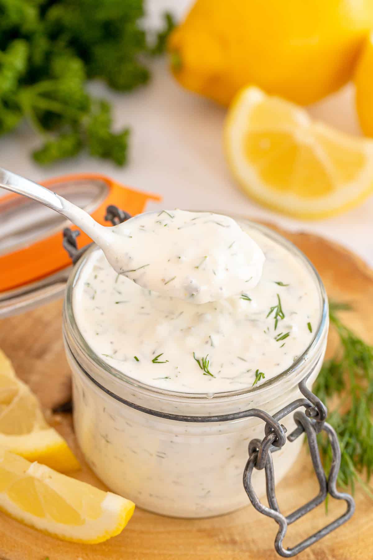 A small spoon scoops tartar sauce from a jar.