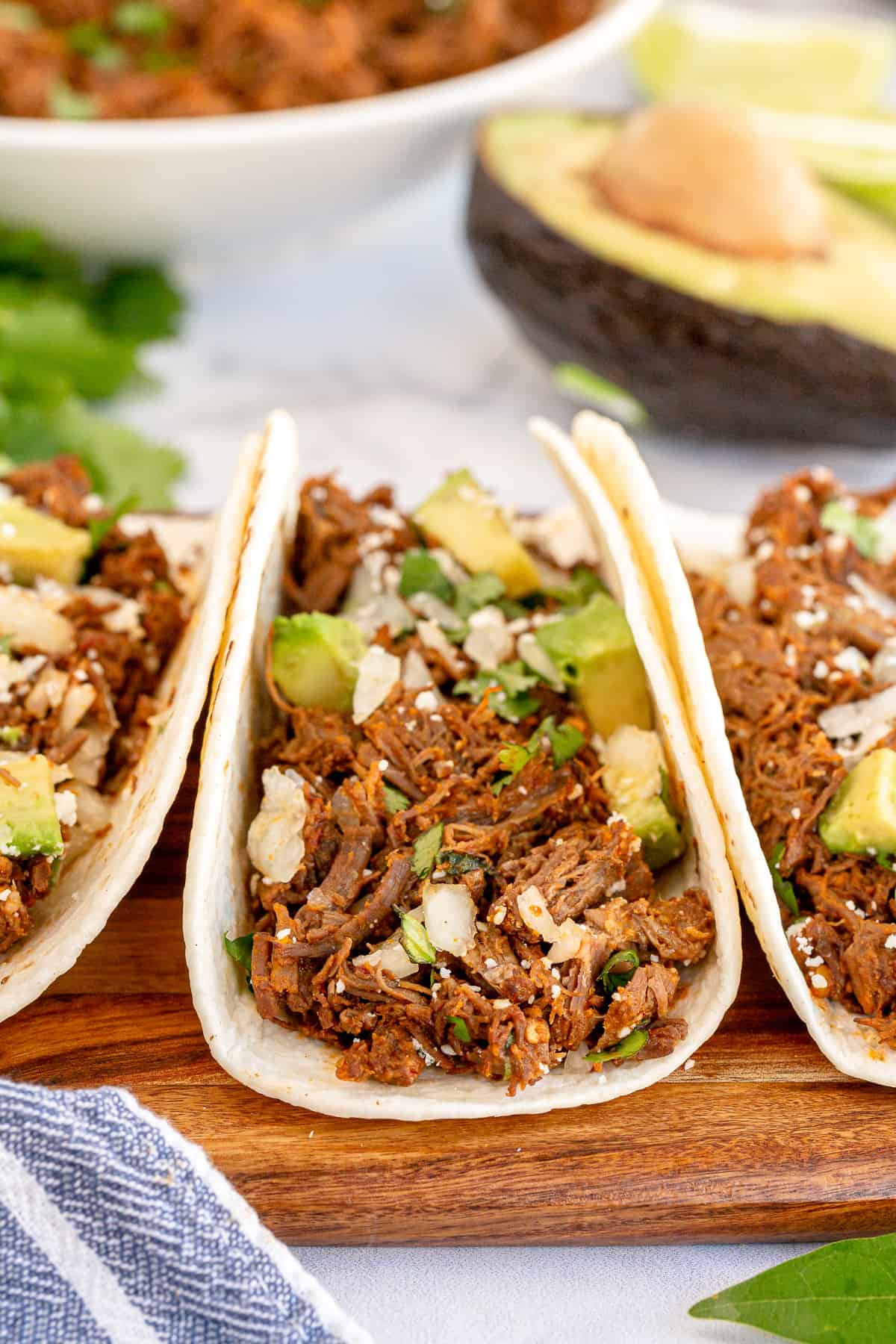 Three barbacoa tacos on a cutting board shot from the side.