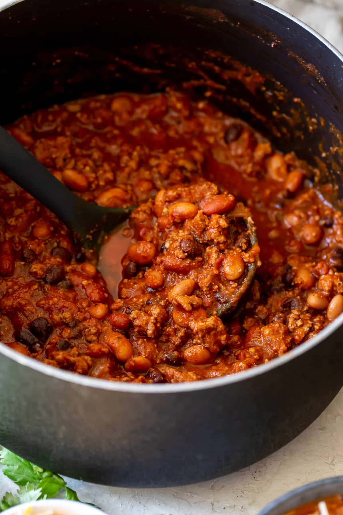 A ladle scooping up turkey chili from a big pot.