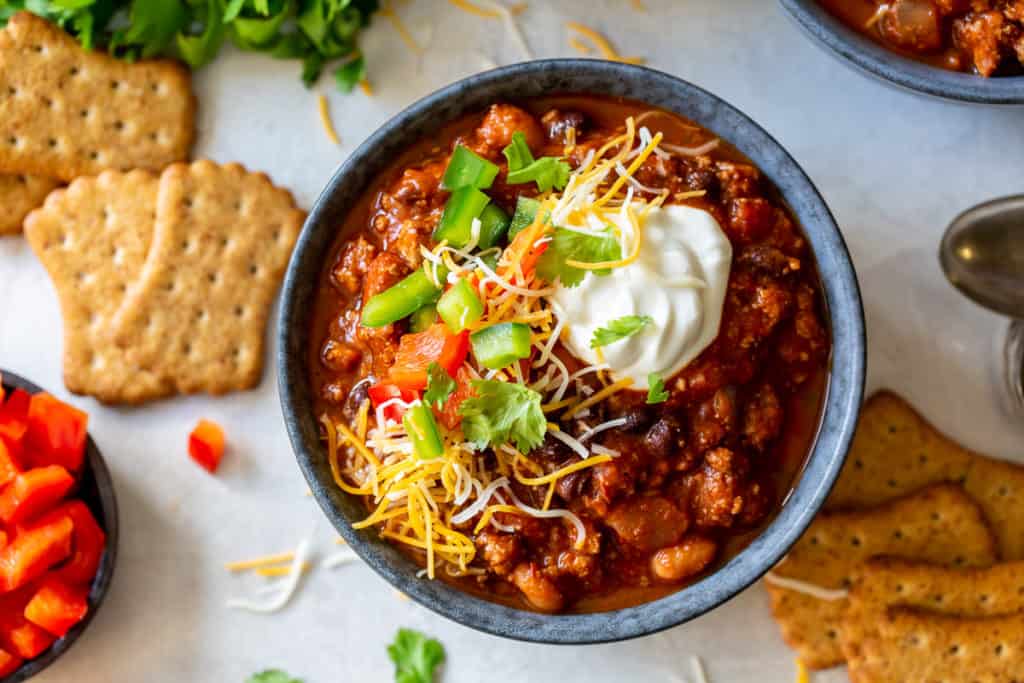 An over the top shot of a bowl of turkey chili topped with cheese and sour cream.
