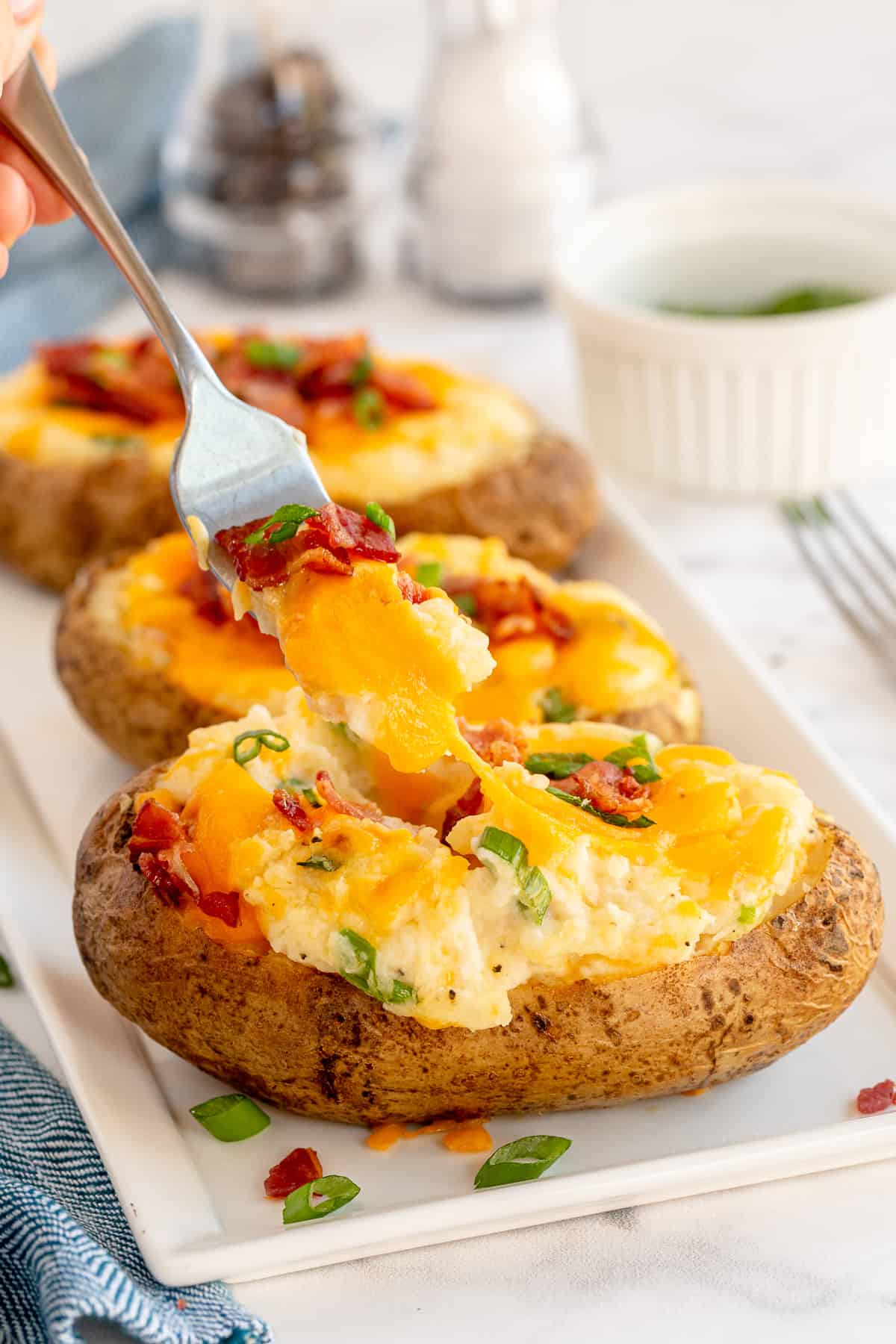 A fork lifts potato and melted cheese from a stuffed potato.