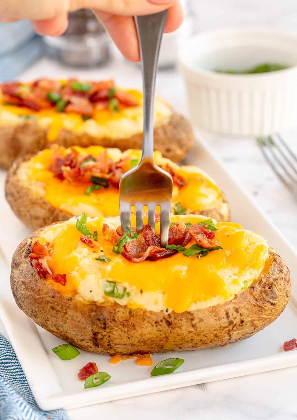 A fork pushes into a potato with cheese and bacon.
