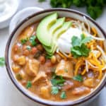 A bowl of chicken chili with cilantro and sour cream in the background.