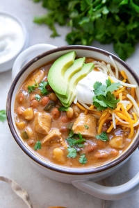 A bowl of chicken chili with cilantro and sour cream in the background.