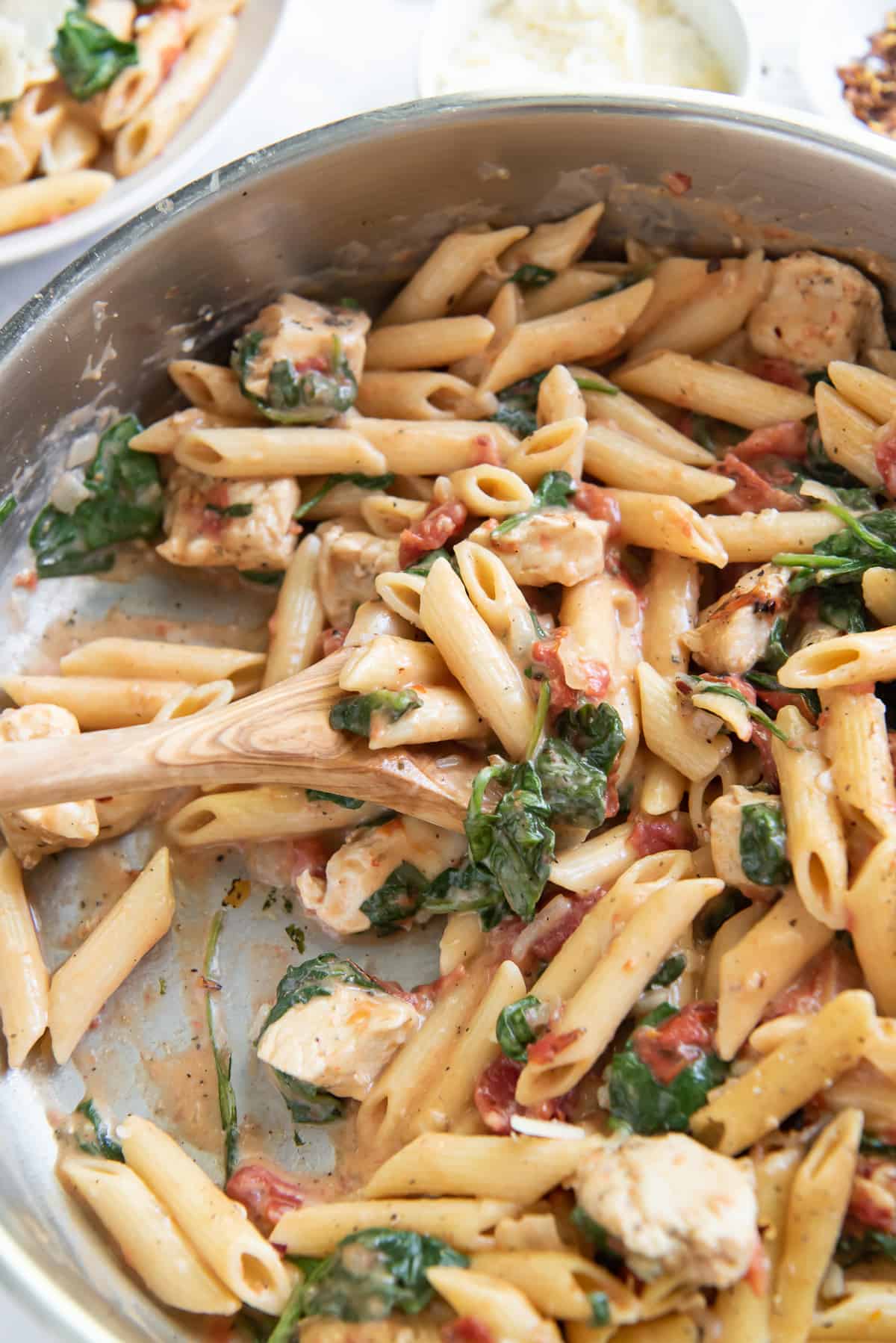 An over the top shot of a wooden spoon scooping pasta in a skillet.