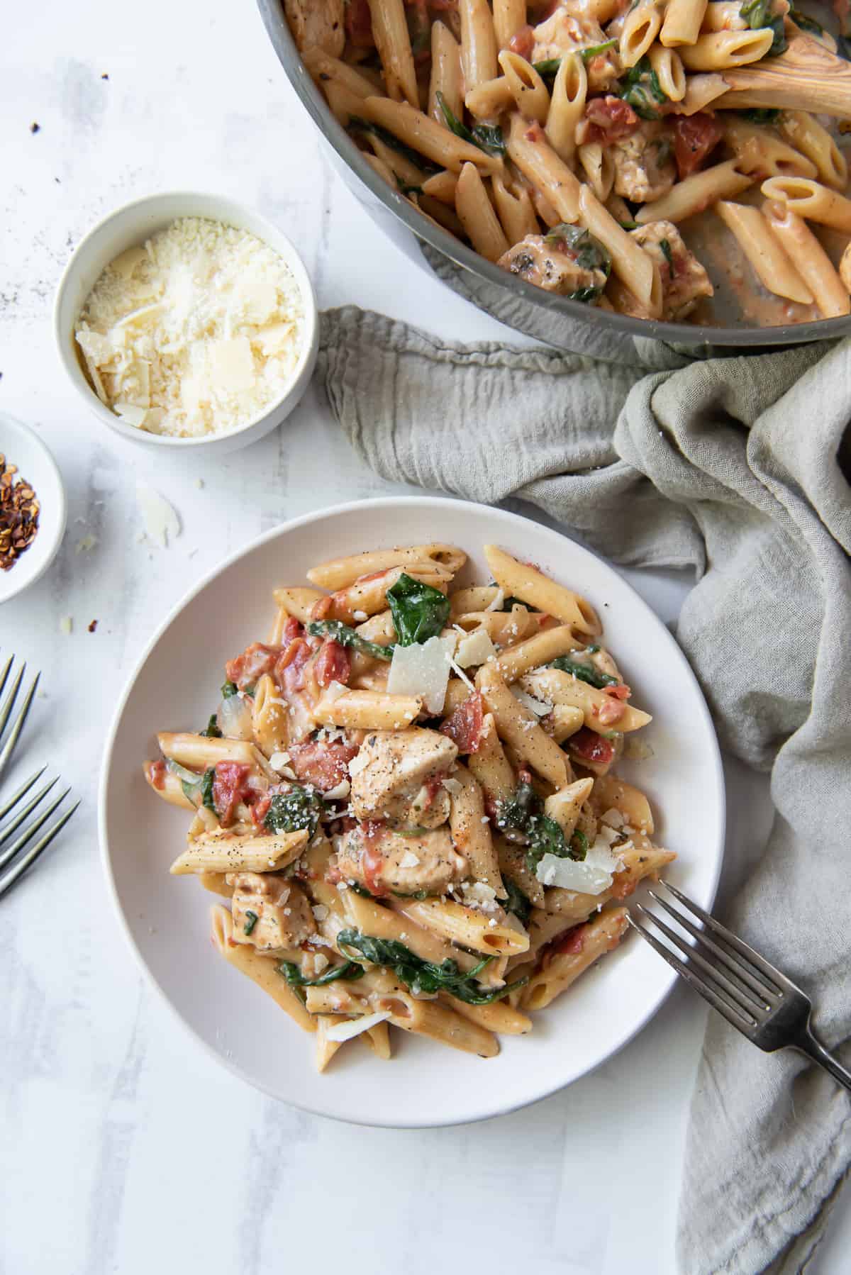 A plate of pasta next to a skillet and small bowl of parmesan.