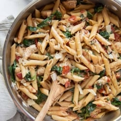 A skillet of pasta with a wooden spoon shot from over the top.