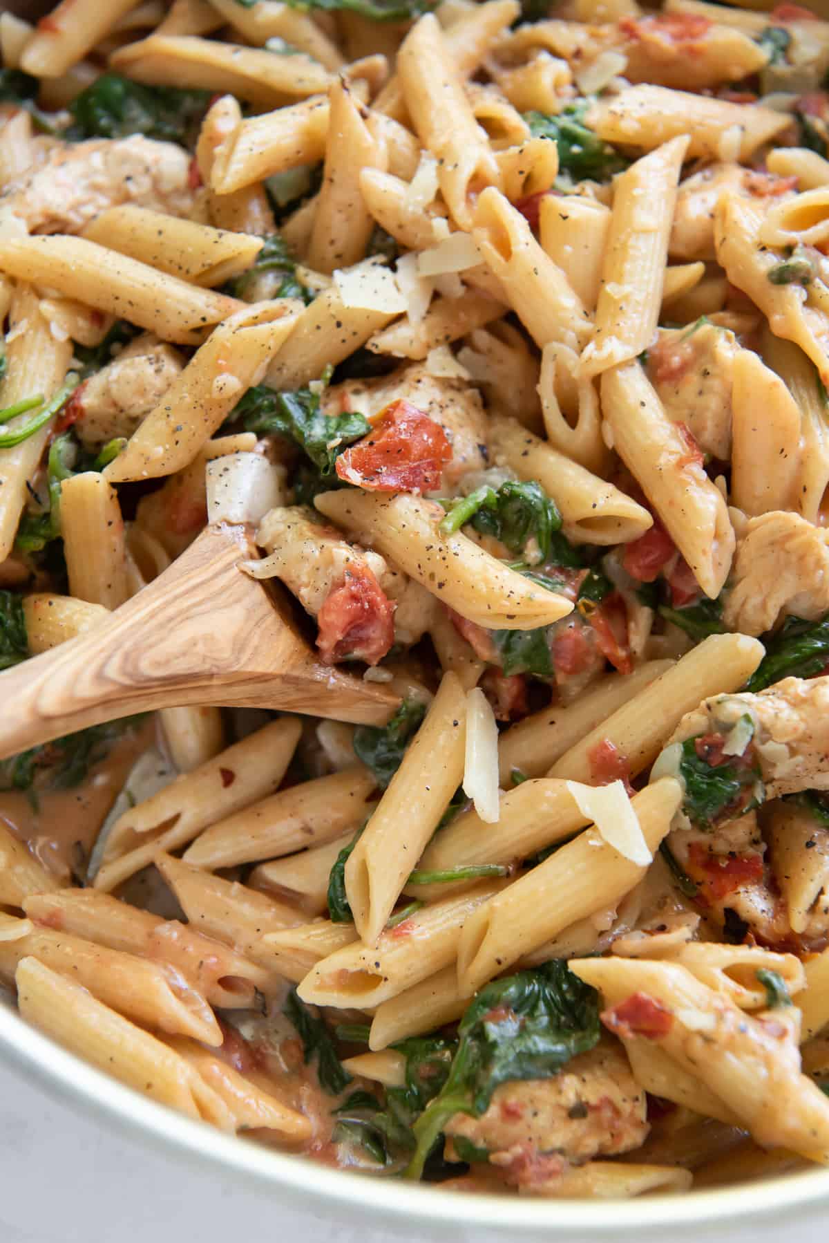 A close up of a spoon in a bowl of pasta with tomatoes, spinach and chicken.